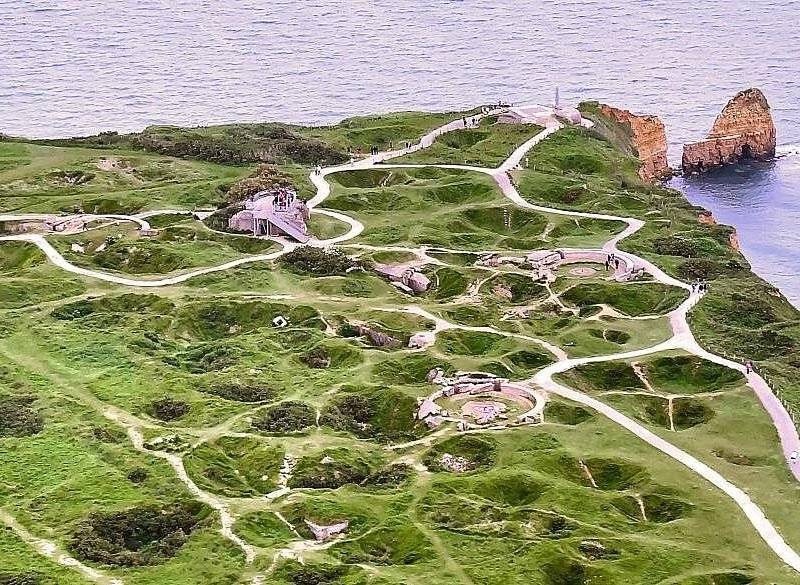 Bomb craters still pitting the grass of a clifftop headland, paths winding between them