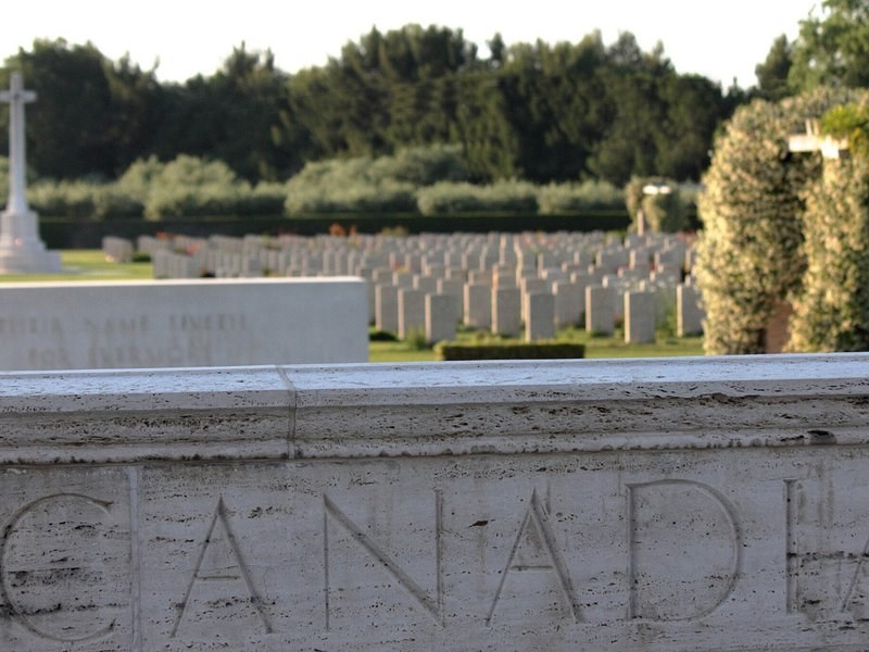Rows of headstones in a Canadian war cemetery behind a wall carved with the word Canada