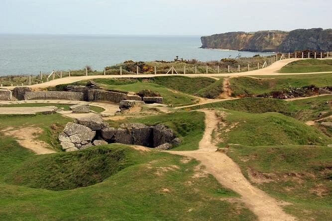 Craters and broken bunkers on a clifftop, the coast running away to the west