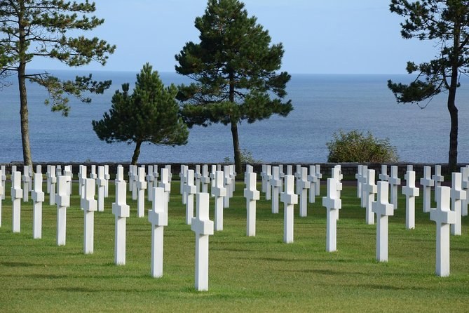 White crosses in rows under tall pines, the Channel behind them