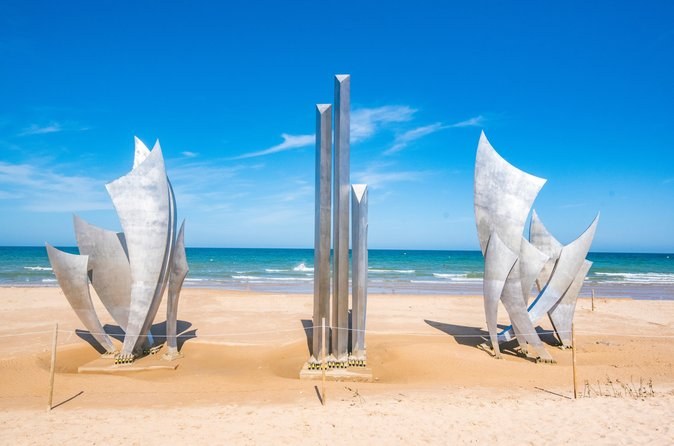Tall steel wings of a memorial sculpture standing on the sand at Omaha Beach