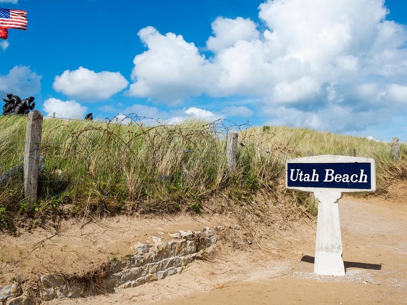 A white Utah Beach marker in the dune grass above the sand